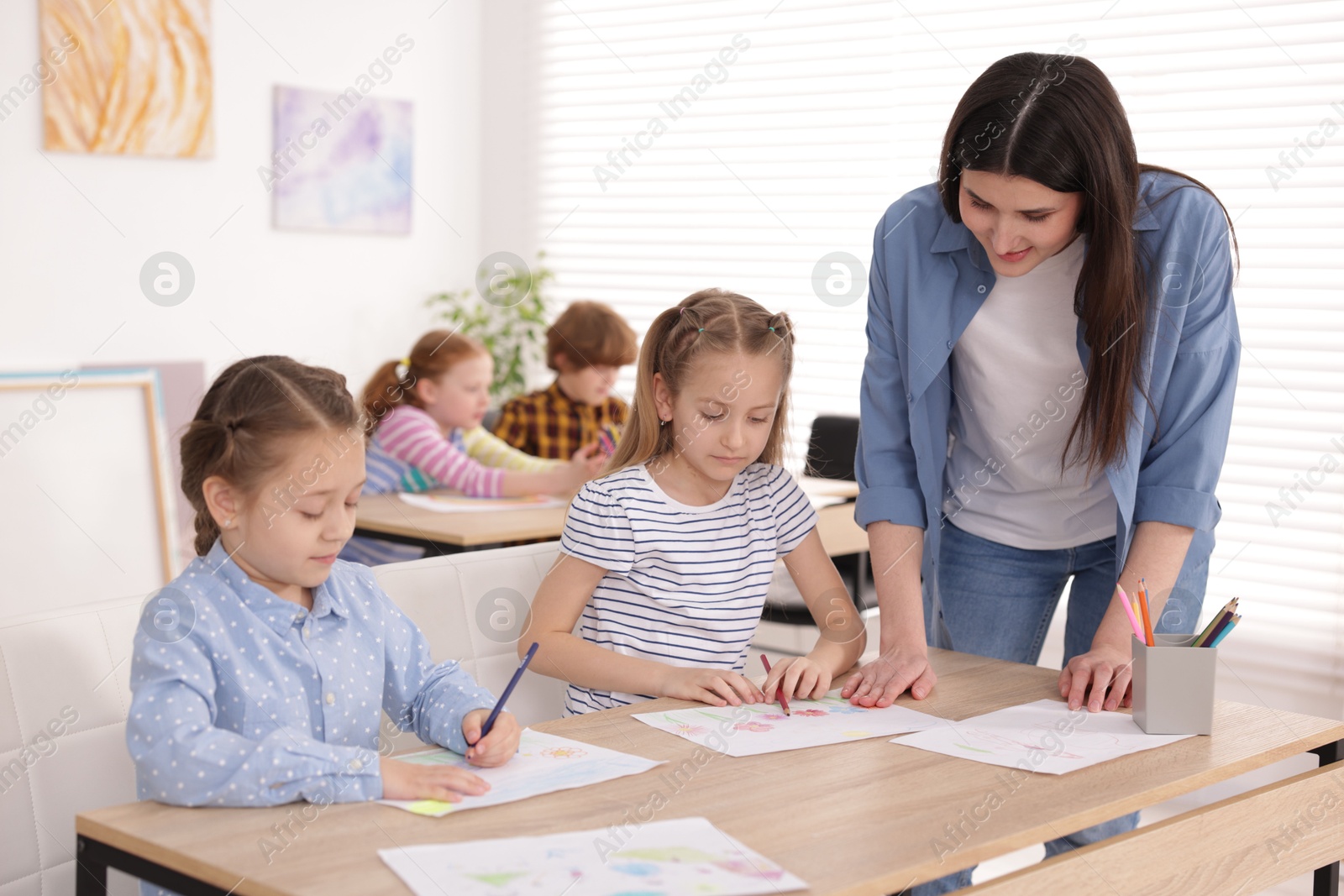 Woman teaching kids to draw at painting lesson indoors, selective focus Photo of Woman teaching kids to draw at painting lesson indoors, selective focus