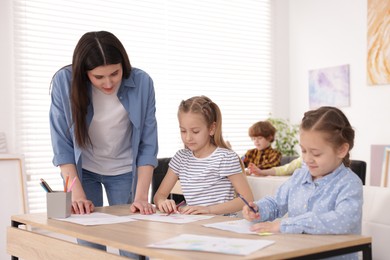 Photo of Woman teaching kids to draw at painting lesson indoors, selective focus
