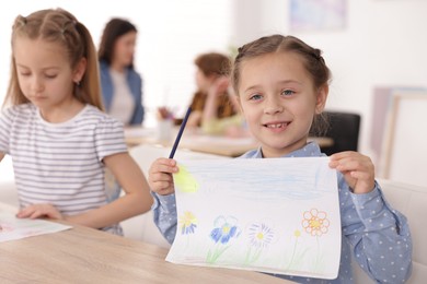 Photo of Cute girl showing her drawing during painting lesson indoors, selective focus