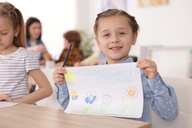 Photo of Cute girl showing her drawing during painting lesson indoors, selective focus