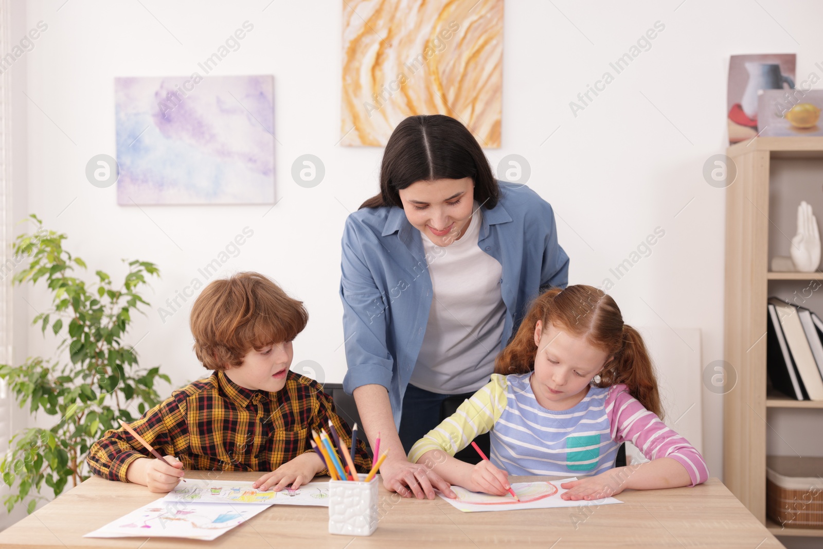 Woman teaching kids to draw at painting lesson indoors Photo of Woman teaching kids to draw at painting lesson indoors