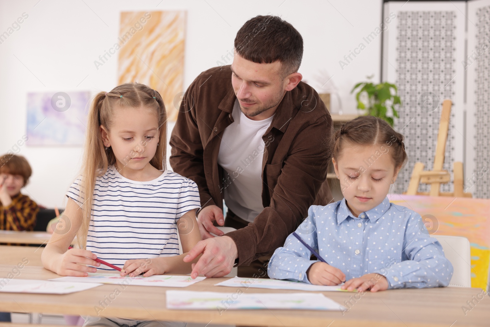 Man teaching kids to draw at painting lesson indoors Photo of Man teaching kids to draw at painting lesson indoors