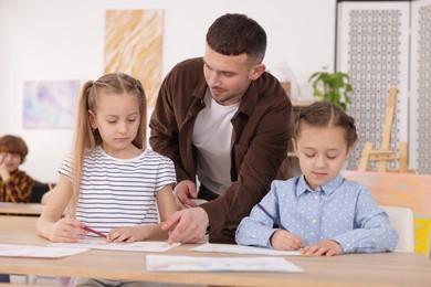Photo of Man teaching kids to draw at painting lesson indoors