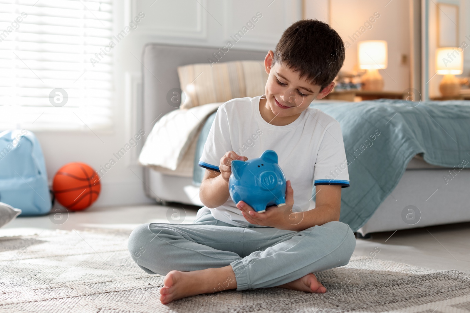 Boy putting pocket money into piggybank at home Photo of Boy putting pocket money into piggybank at home