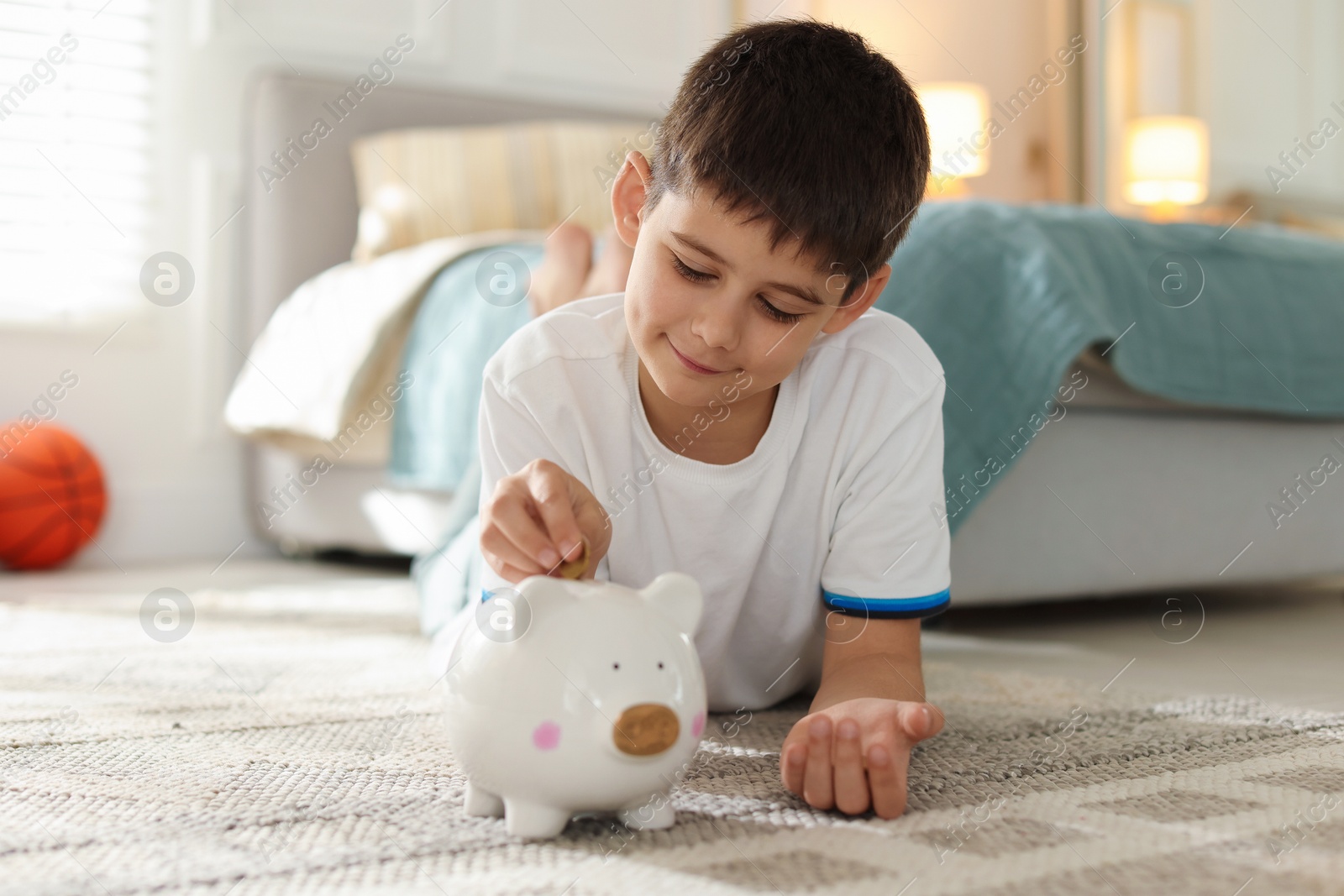 Boy putting pocket money into piggybank at home Photo of Boy putting pocket money into piggybank at home