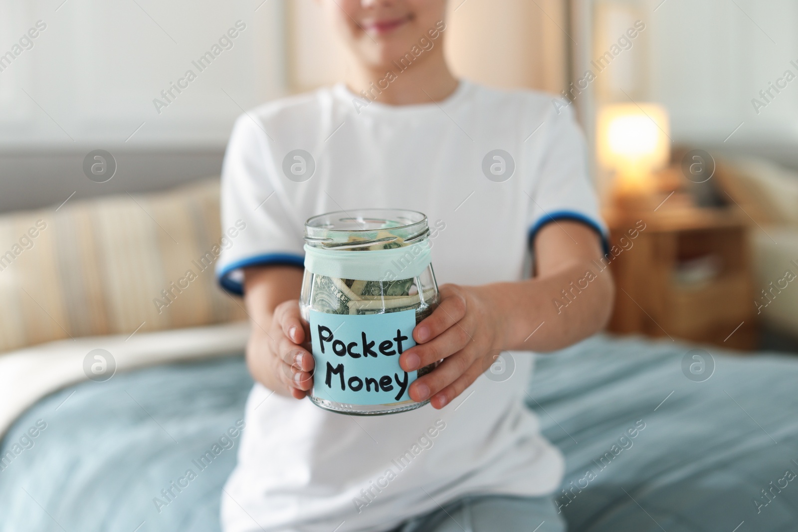 Boy with jar of pocket money on bed at home, closeup Photo of Boy with jar of pocket money on bed at home, closeup