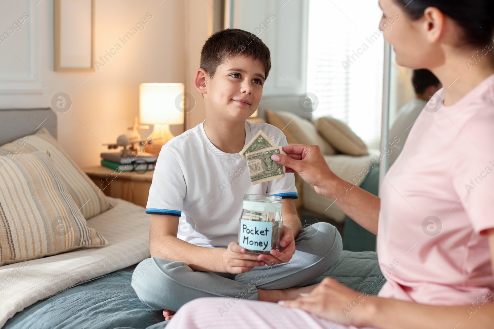Mother and son putting pocket money into jar at home, closeup Photo of Mother and son putting pocket money into jar at home, closeup
