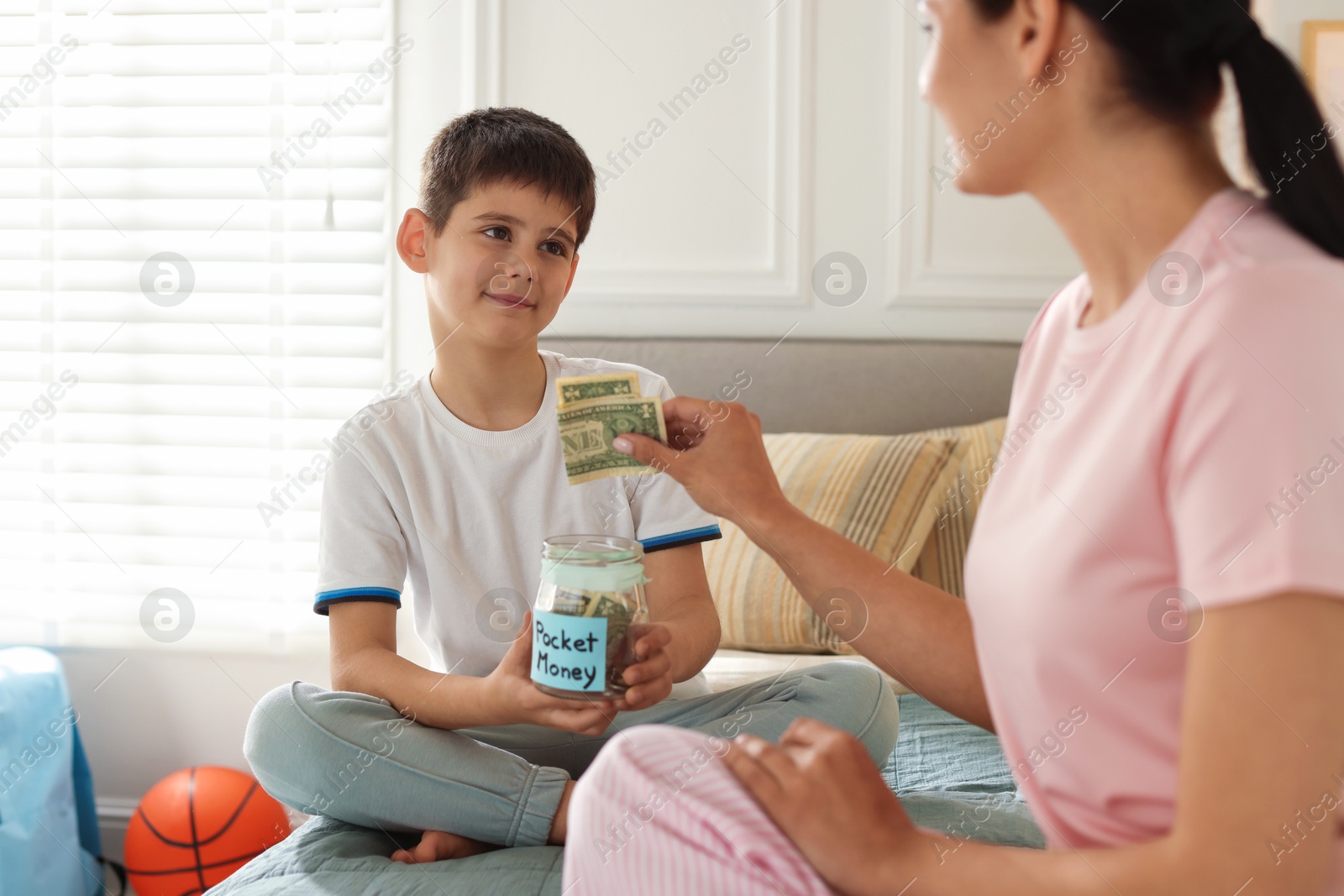 Mother and son putting pocket money into jar at home, closeup Photo of Mother and son putting pocket money into jar at home, closeup
