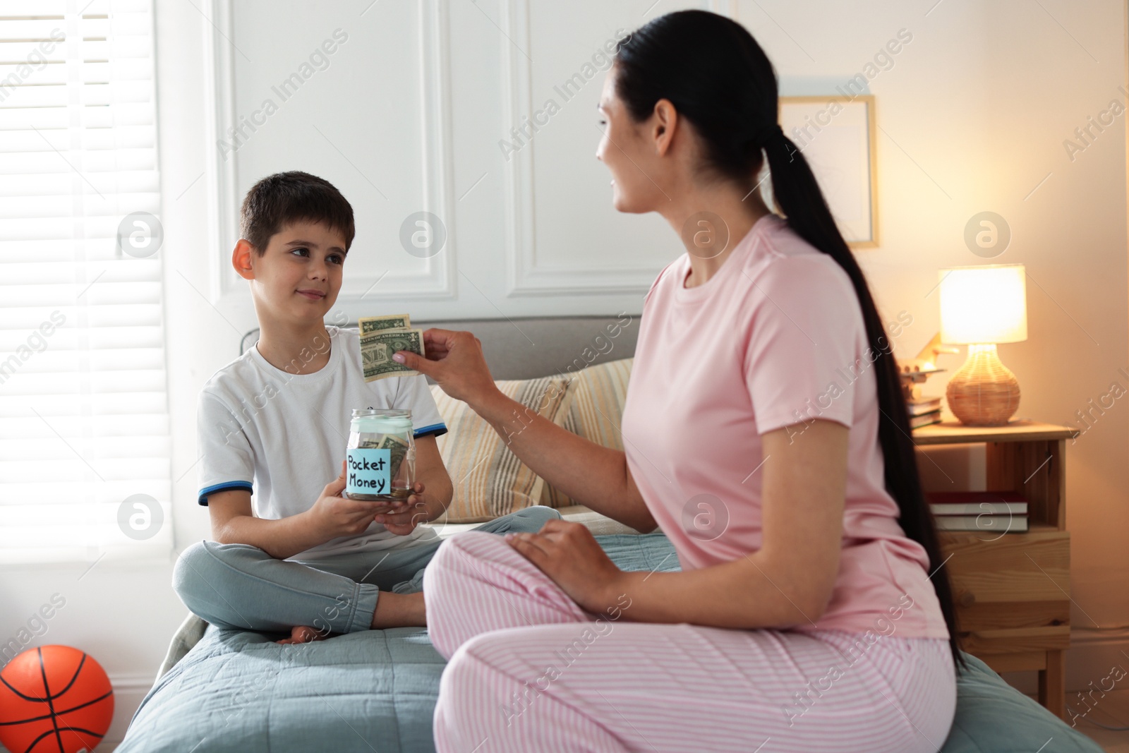 Mother and son putting pocket money into jar at home Photo of Mother and son putting pocket money into jar at home