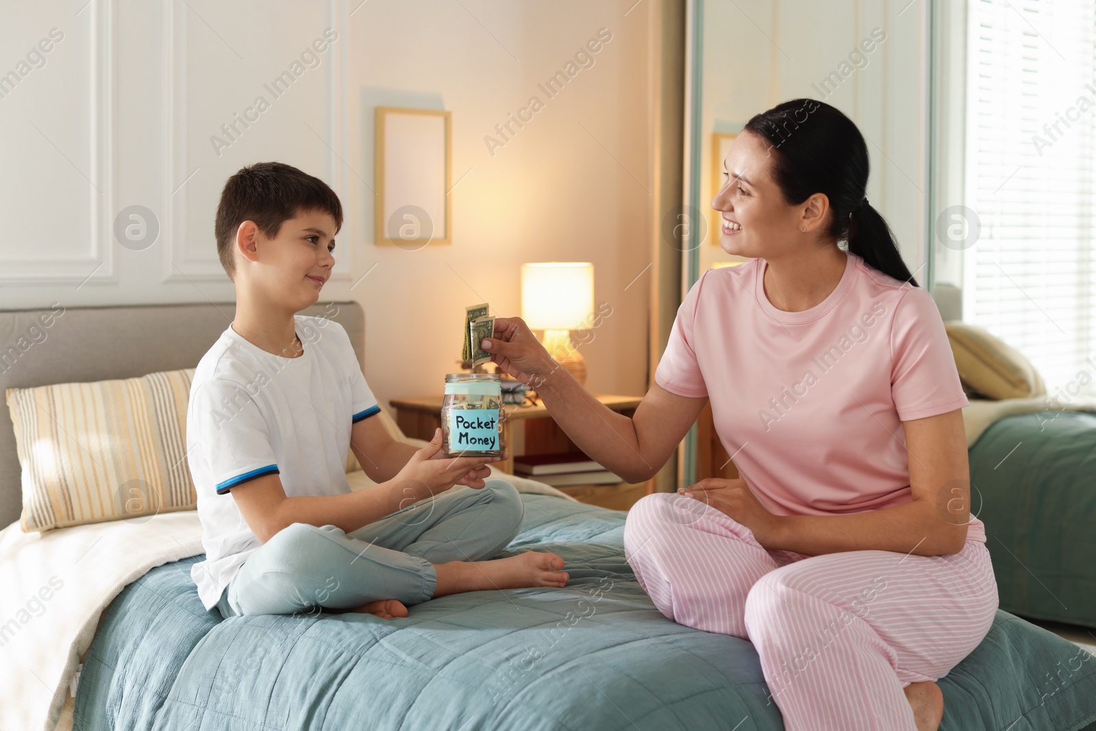 Mother and son putting pocket money into jar at home Photo of Mother and son putting pocket money into jar at home