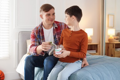 Photo of Father and son putting pocket money into jar at home