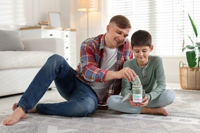 Photo of Father and son putting pocket money into jar at home