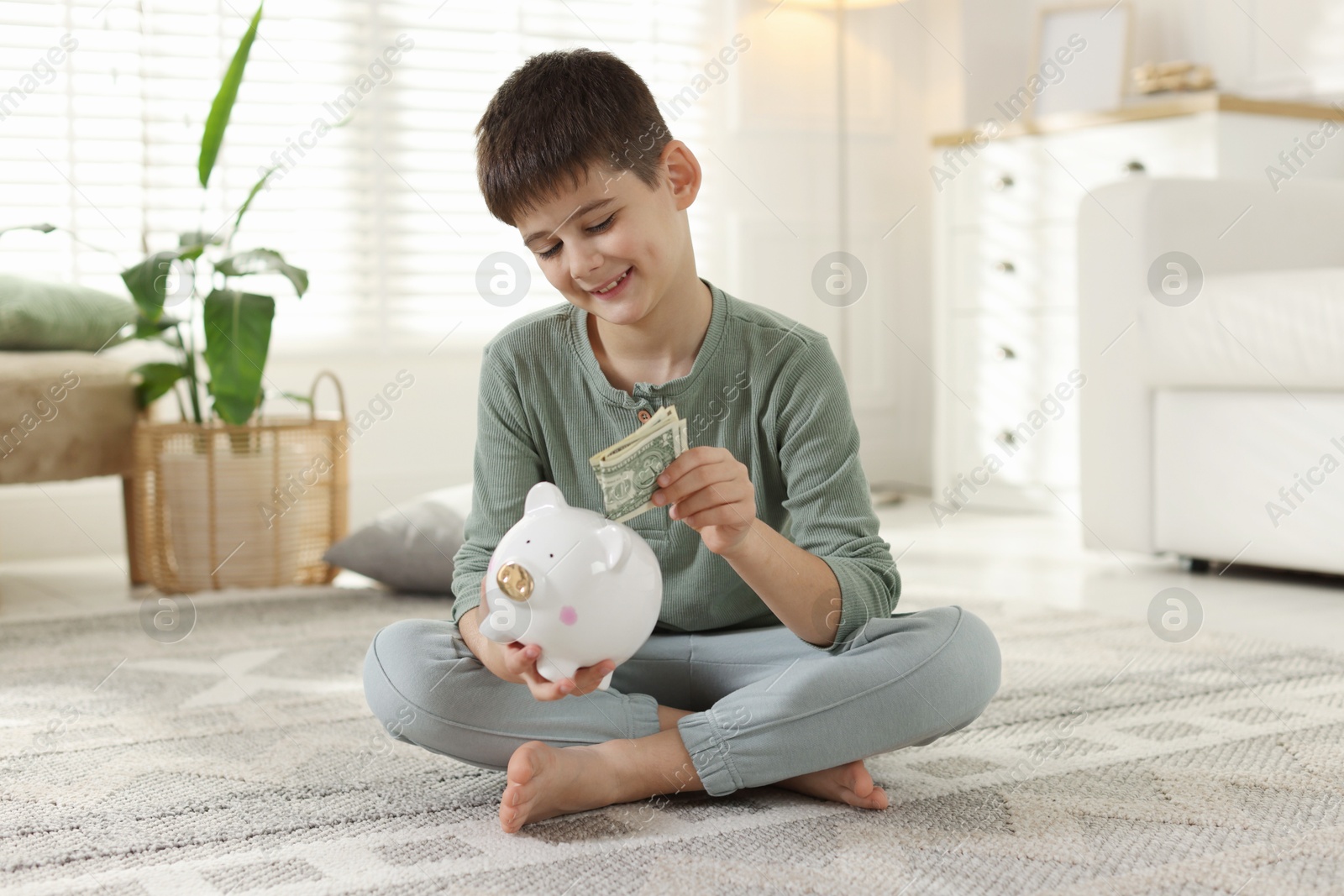 Boy putting pocket money into piggybank at home Photo of Boy putting pocket money into piggybank at home