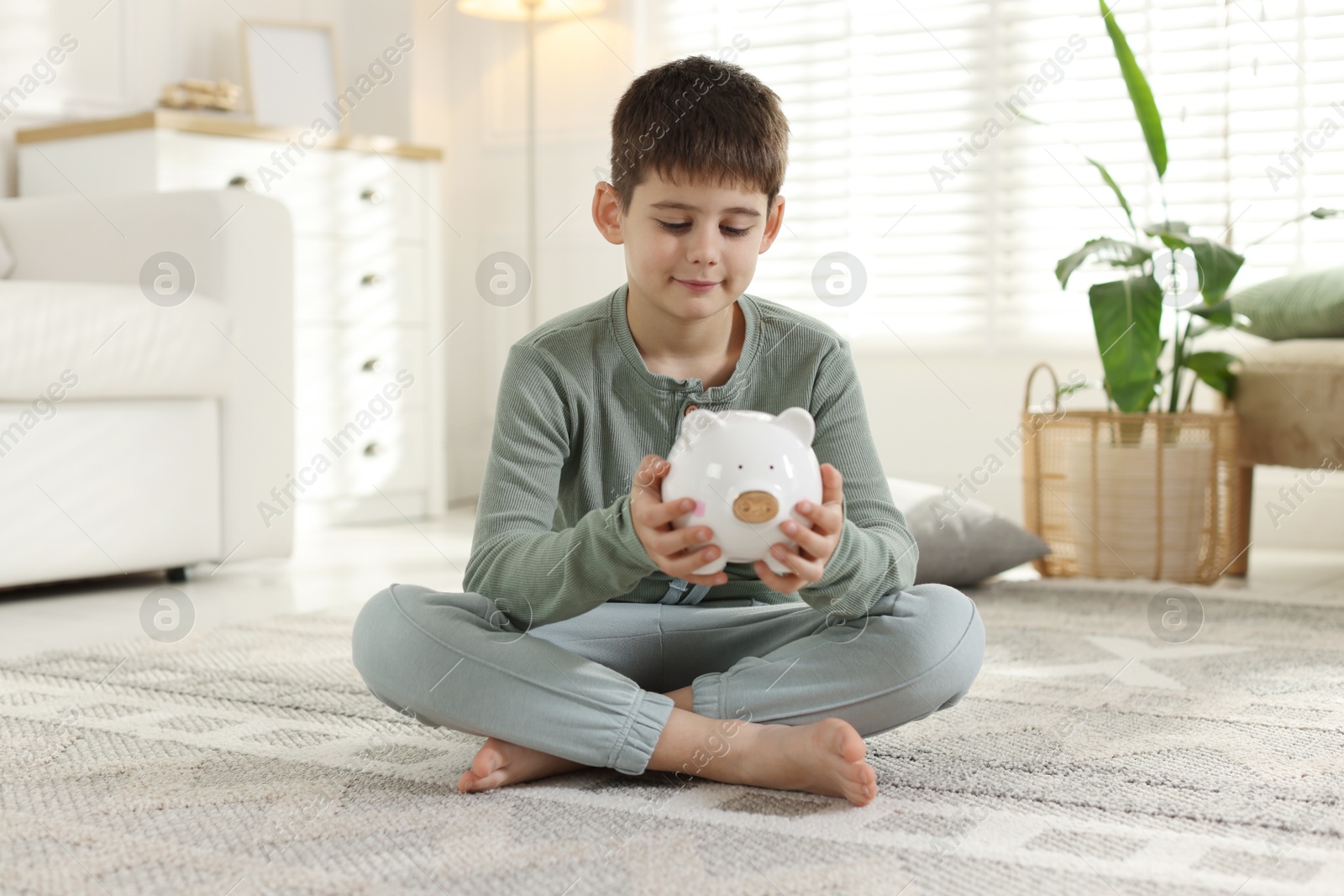 Boy with piggybank of pocket money at home Photo of Boy with piggybank of pocket money at home