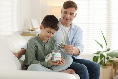 Photo of Dad giving his son pocket money on sofa at home
