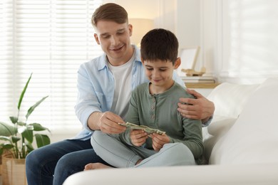 Photo of Dad giving his son pocket money on sofa at home