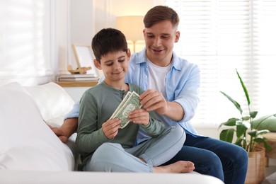 Photo of Dad giving his son pocket money on sofa at home