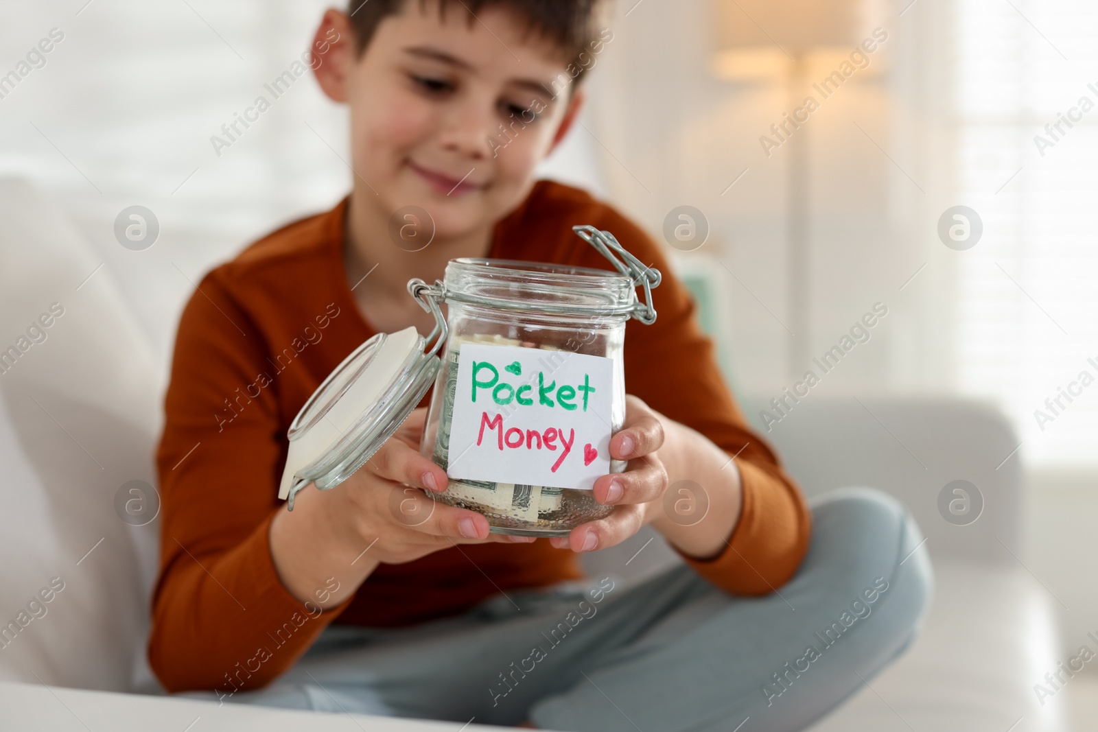 Boy with jar of pocket money on sofa at home, selective focus Photo of Boy with jar of pocket money on sofa at home, selective focus