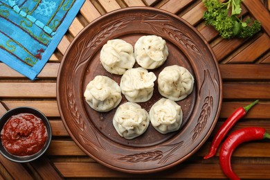 Photo of Delicious khinkali served with sauce on wooden table, flat lay