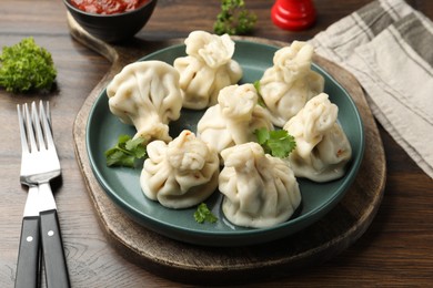 Photo of Delicious khinkali served with cilantro on wooden table, closeup