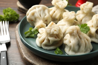 Photo of Delicious khinkali served with cilantro on wooden table, closeup