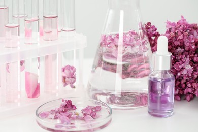 Photo of Making luxury perfume. Essential oils in glassware and flowers on white table, closeup