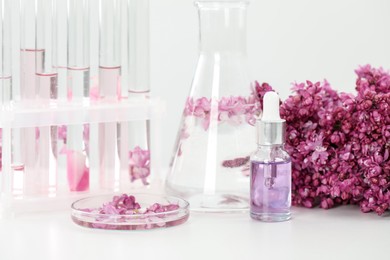 Photo of Making luxury perfume. Essential oils in glassware and flowers on white table, closeup