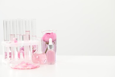 Photo of Making luxury perfume. Essential oils in glassware and flowers on white table, space for text