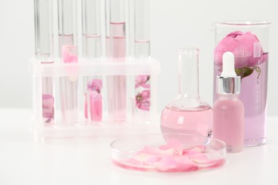 Photo of Making luxury perfume. Essential oils in glassware and flowers on white table, closeup