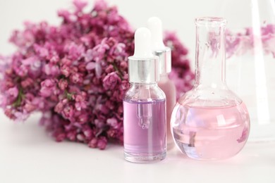 Photo of Making luxury perfume. Essential oils in glassware and flowers on white table, closeup
