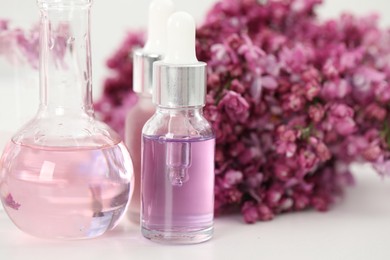 Photo of Making luxury perfume. Essential oils in glassware and flowers on white table, closeup