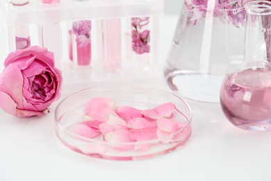 Photo of Making luxury perfume. Essential oils in glassware and flowers on white table, closeup