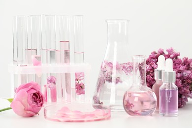 Photo of Making luxury perfume. Essential oils in glassware and flowers on white table, closeup