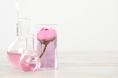Photo of Making luxury perfume. Essential oils in glassware and flowers on white wooden table, closeup. Space for text