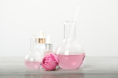 Photo of Making luxury perfume. Essential oils in glassware and flowers on white wooden table, closeup