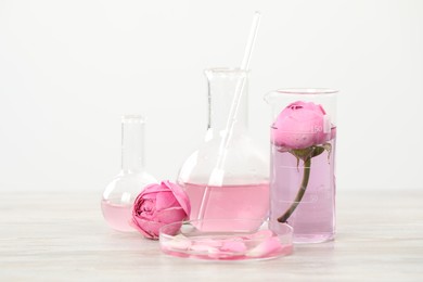 Photo of Making luxury perfume. Essential oils in glassware and flowers on white wooden table, closeup