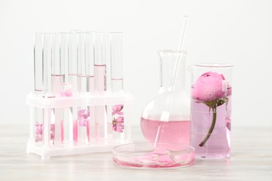 Photo of Making luxury perfume. Essential oils in glassware and flowers on white wooden table, closeup