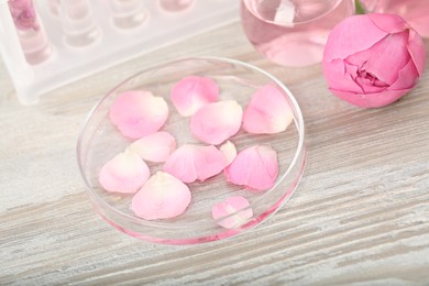 Photo of Making luxury perfume. Essential oils in glassware and flowers on white wooden table, closeup