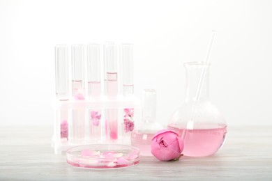 Photo of Making luxury perfume. Essential oils in glassware and flowers on white wooden table, closeup
