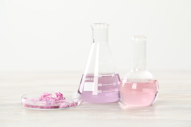 Photo of Making luxury perfume. Essential oils in glassware and flowers on white wooden table, closeup