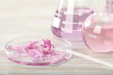 Photo of Making luxury perfume. Essential oils in glassware and flowers on white wooden table, closeup