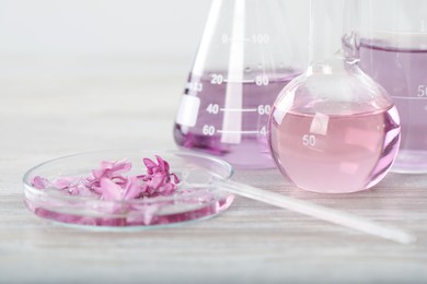 Photo of Making luxury perfume. Essential oils in glassware and flowers on white wooden table, closeup