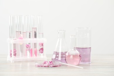 Photo of Making luxury perfume. Essential oils in glassware and flowers on white wooden table, closeup