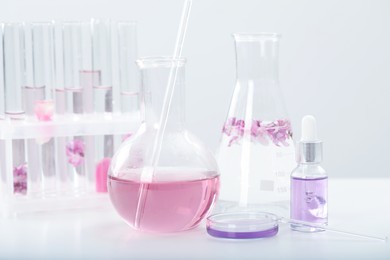 Photo of Making luxury perfume. Essential oils in glassware and flowers on white table, closeup