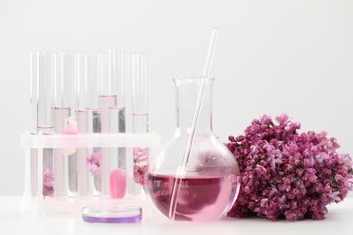 Photo of Making luxury perfume. Essential oils in glassware and flowers on white table, closeup