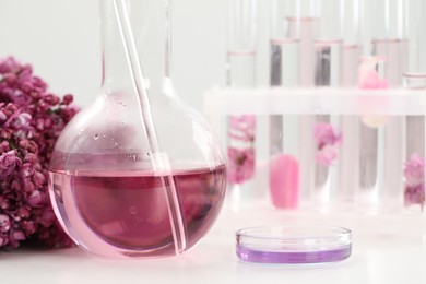 Photo of Making luxury perfume. Essential oils in glassware and flowers on white table, closeup