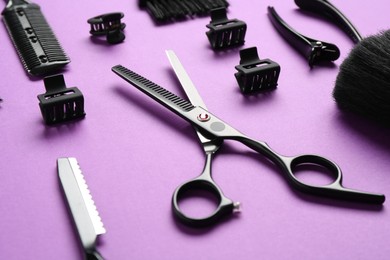 Photo of Different hairdresser's tools on violet background, closeup