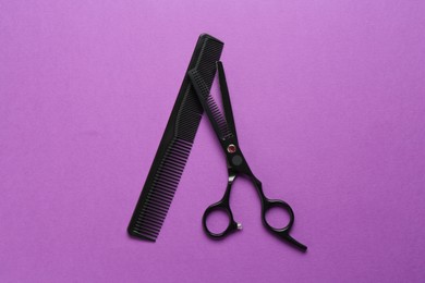 Photo of Scissors and comb on violet background, flat lay. Hairdresser's tools
