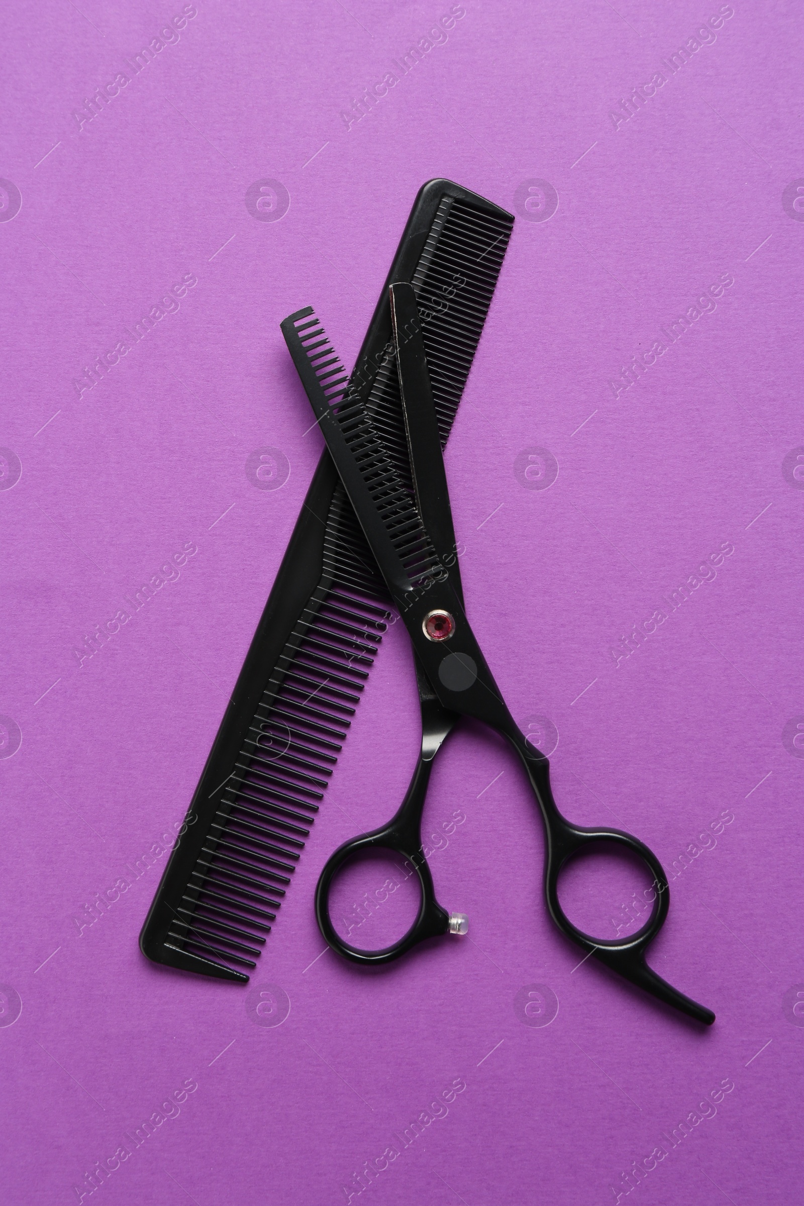 Photo of Scissors and comb on violet background, flat lay. Hairdresser's tools
