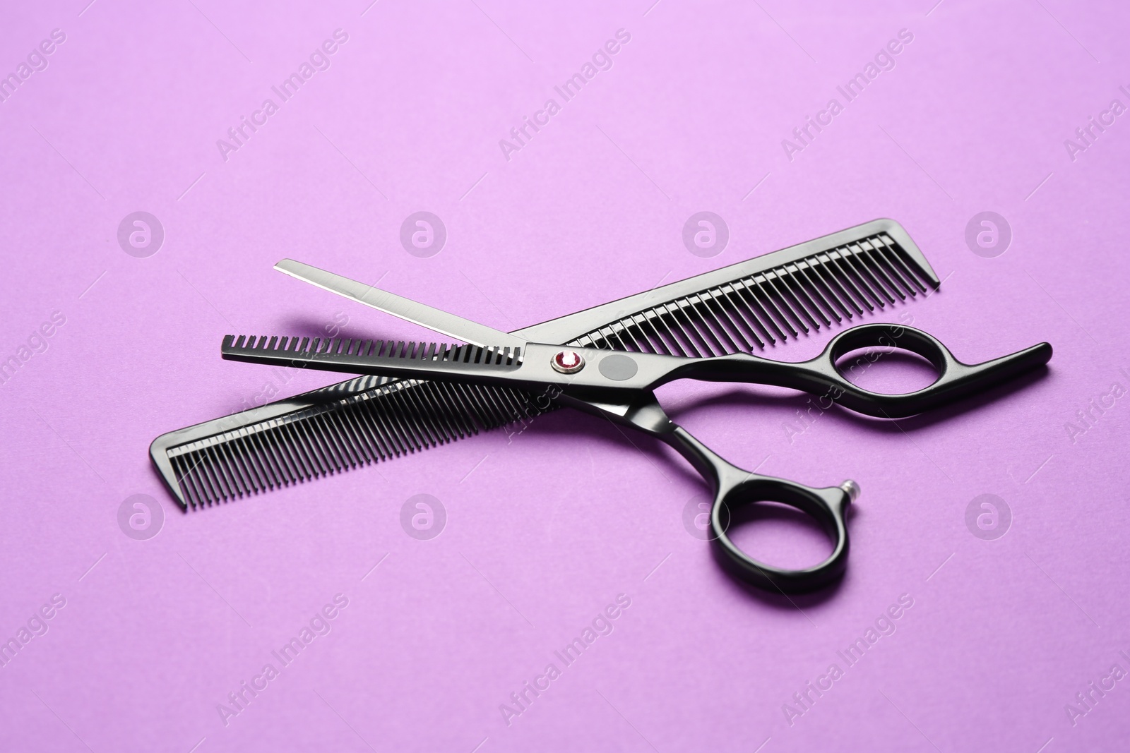 Photo of Scissors and comb on violet background, closeup. Hairdresser's tools